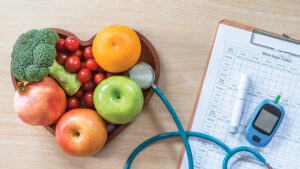 fruit and veggies in a heart bowl with a stethoscope and a blood sugar monitor on a clip board with a chart